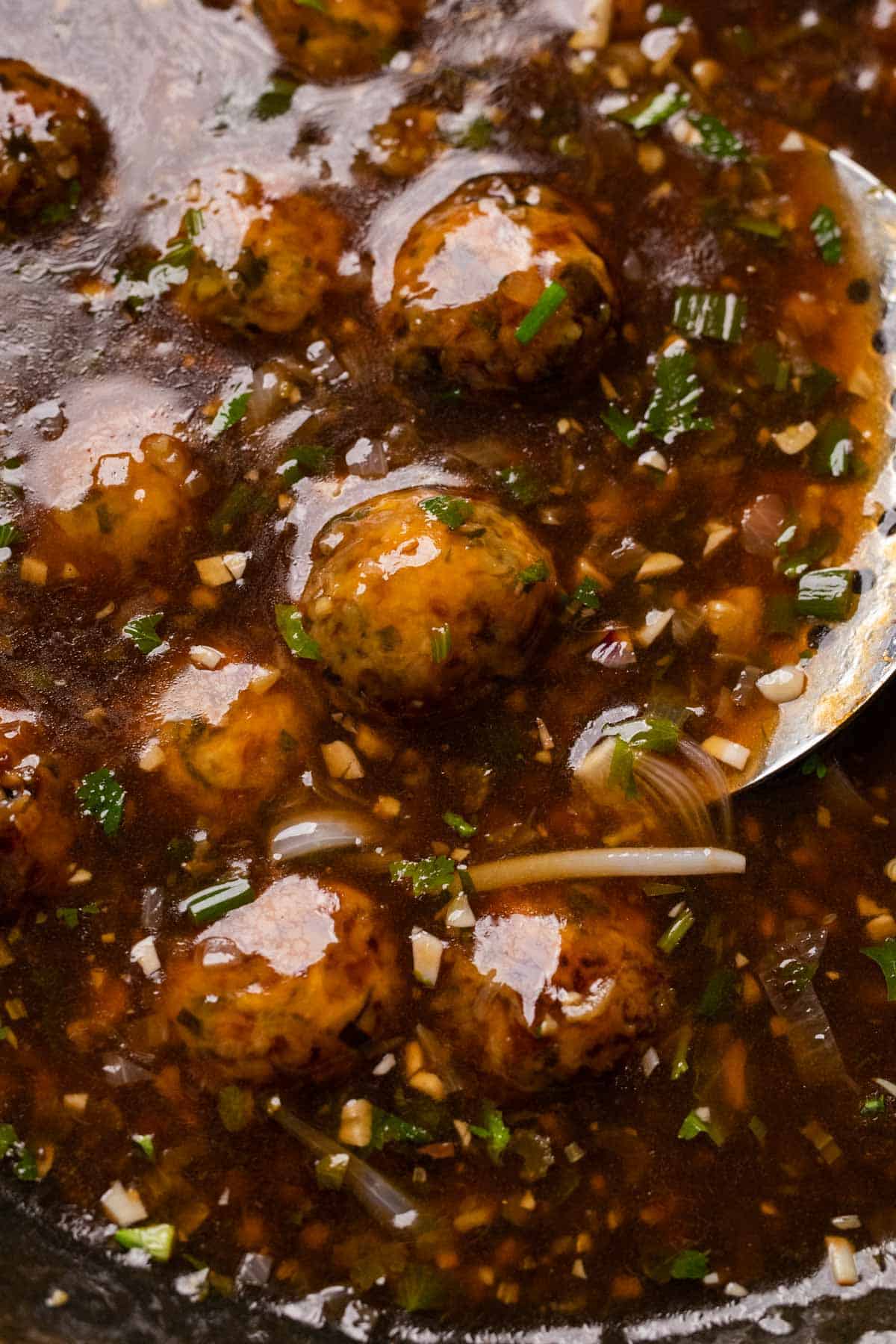 Closeup of veg manchurian in a wok with a perforated spoon on the side