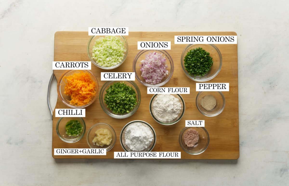 All the ingredients required for veg balls pictured on a wooden chopping board with text to identify them
