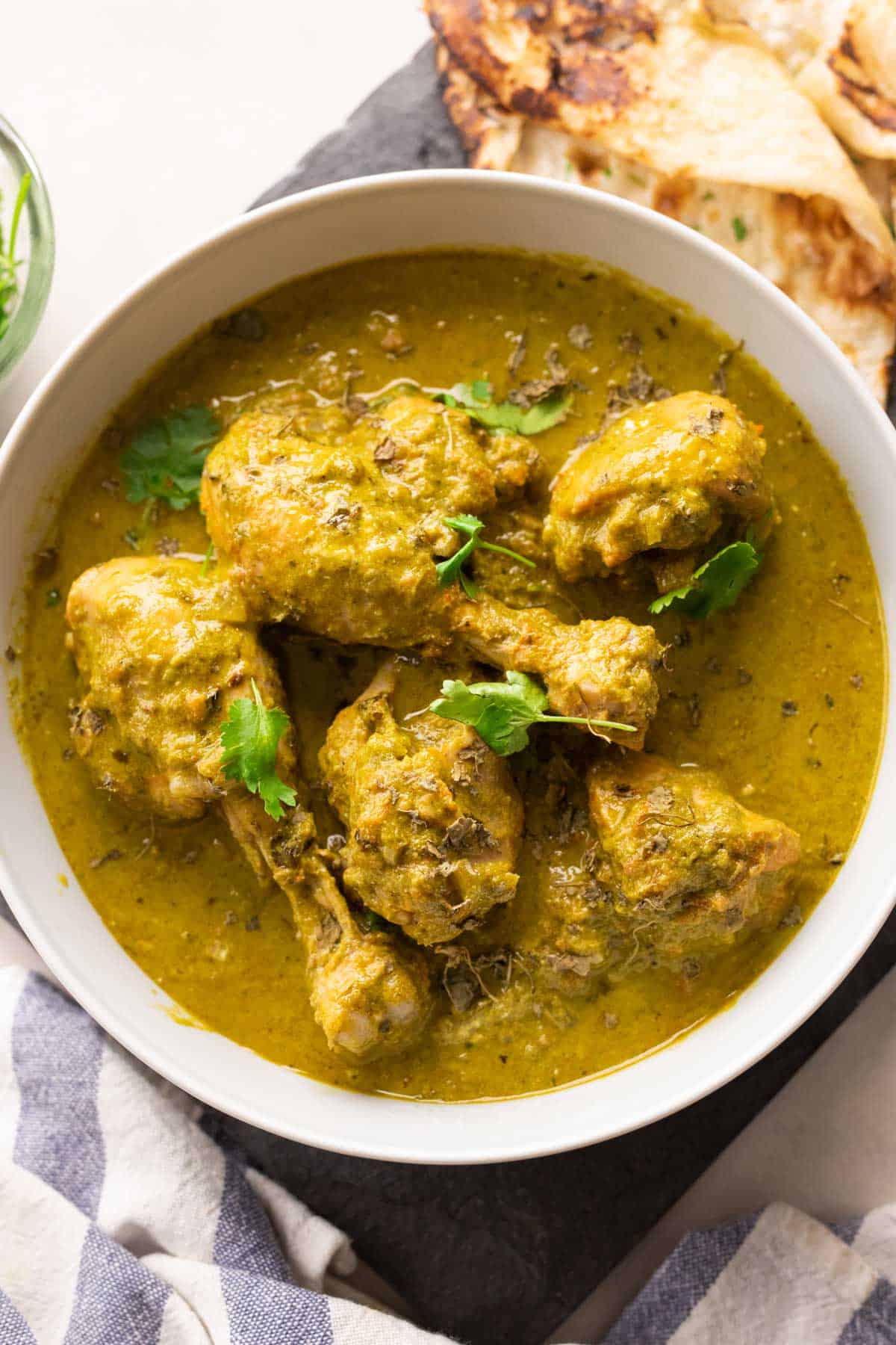 Picture of saag chicken served in a white bowl with naan on the side