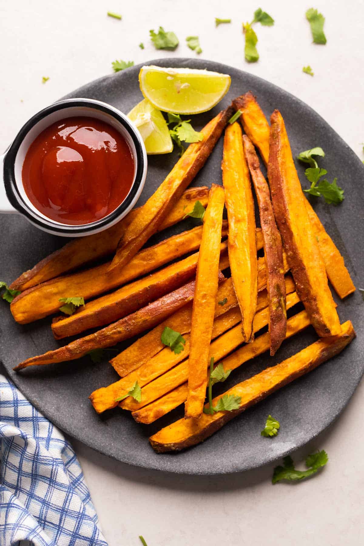 Picture of baked sweet potato fries served on a grey plate with ketchup and lime wedges on the side