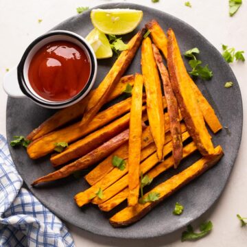 Picture of baked sweet potato fries served on a grey plate with ketchup and lime wedges on the side