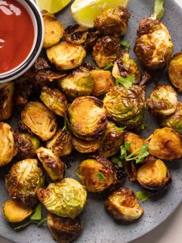 Roasted air fryer brussel sprouts served on a grey plate with ketchup on the side
