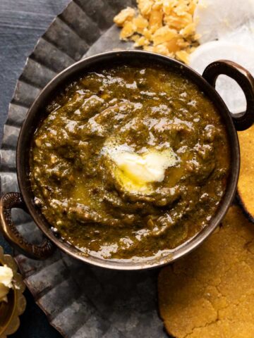Picture of sarson ka saag served in a small copper kadhai with makki roti on the side