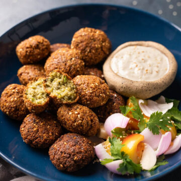 Crispy falafels served in a blue bowl with tahini dip and salad on the side