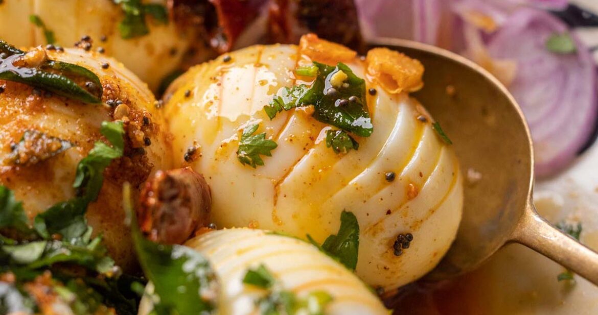 Close up of hasselback egg tadka with a spoon and sliced onions on the side