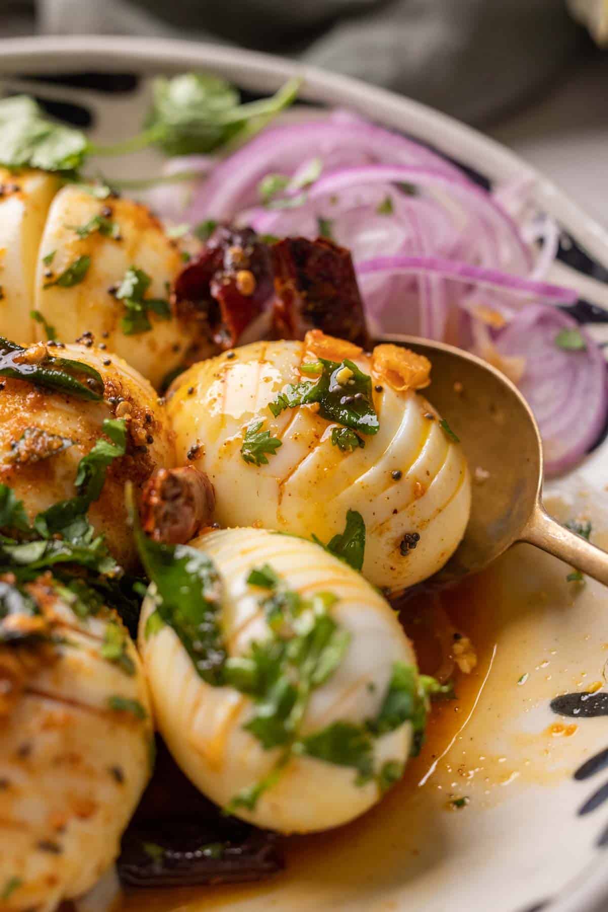 Close up of hasselback egg tadka with a spoon and sliced onions on the side