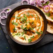 Picture of shahi paneer served in a black bowl with onions and naan on the side