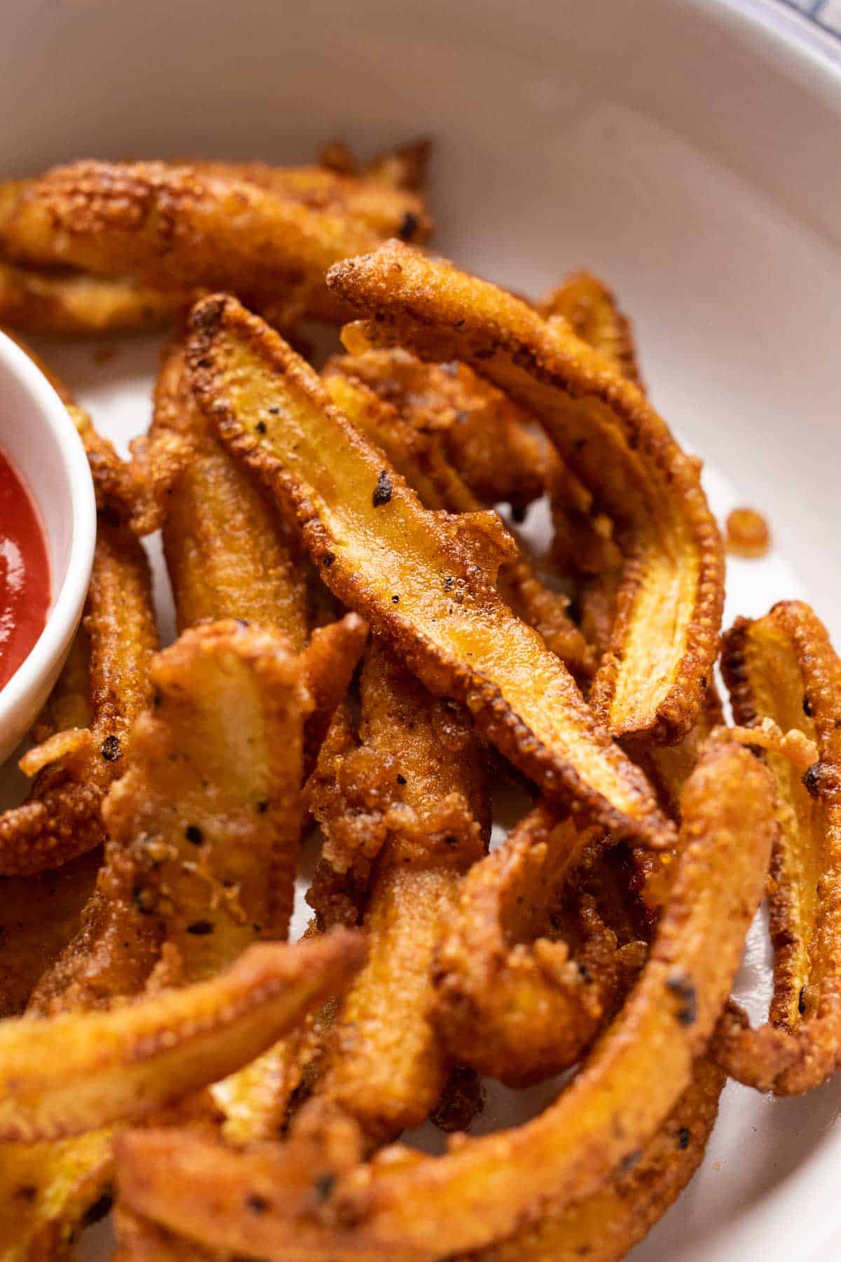 Closeup of crispy baby corn fry served in a white plate with ketchup on the side