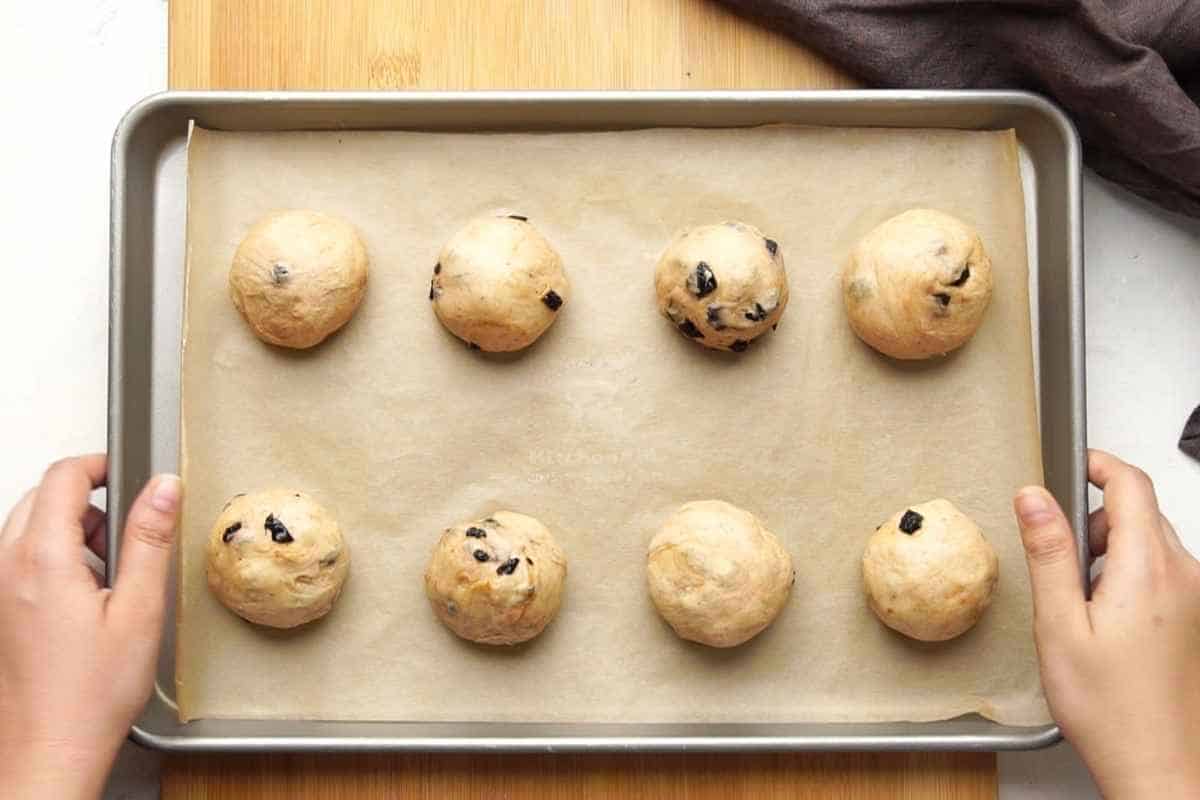 the dough rolled into multiple balls placed on brown paper in a baking pan