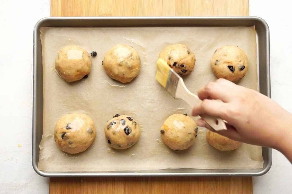 buttering the the dough rolled into multiple balls placed on brown paper in a baking pan