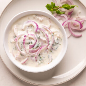 Picture of onion raita served in a white bowl on a white plate