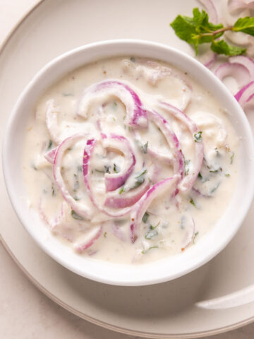 Picture of onion raita served in a white bowl on a white plate
