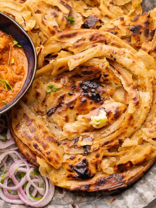 Lachha Parathas served on a plate with curry and onions