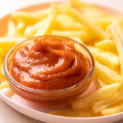A bowl of ketchup placed on a plate with french fries