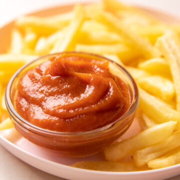 A bowl of ketchup placed on a plate with french fries