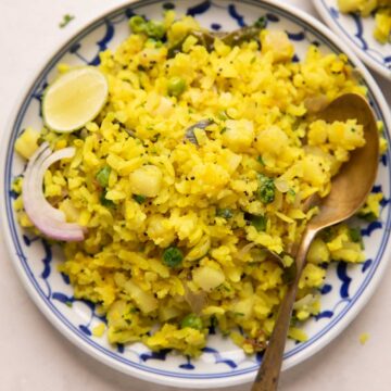Poha served in a plate with sliced onion and a lime wedge on the side
