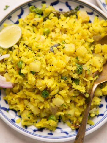 Poha served in a plate with sliced onion and a lime wedge on the side
