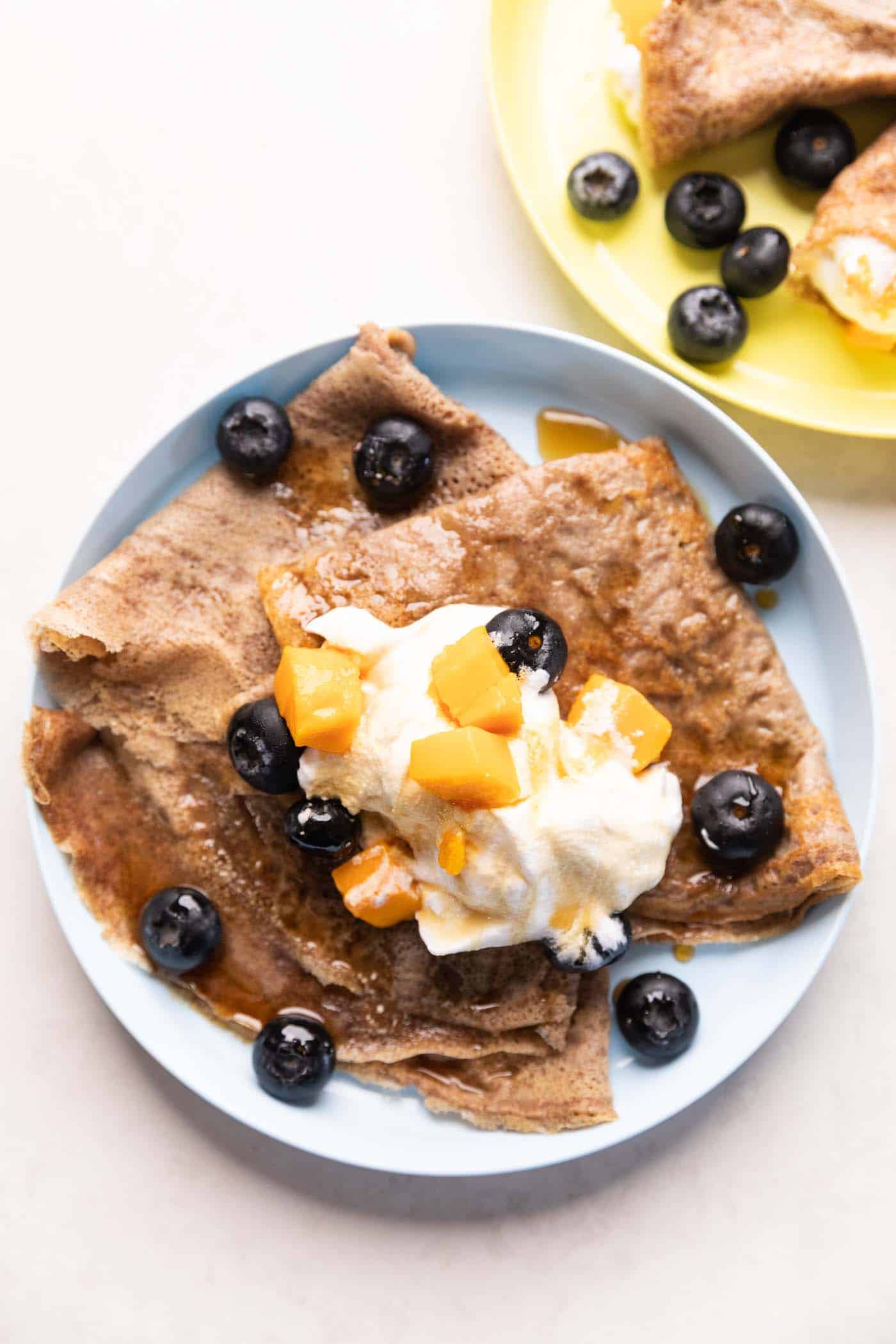 Ragi Crepes served on a plate topped with whipped cream, mango and blueberries