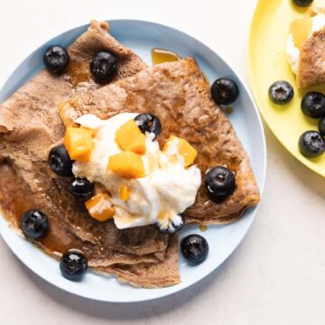 Ragi Crepes served on a plate topped with whipped cream, mango and blueberries