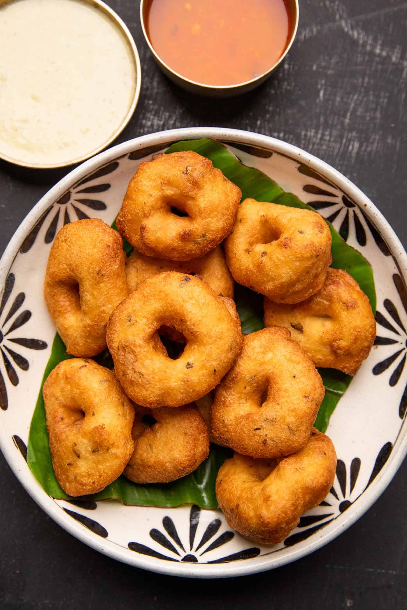 Medu vada served over a banana leaf in a bowl with chutney and sambar on the side
