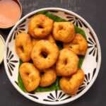 Medu vada served over a comic leaf in a trencher with chutney and sambar on the side