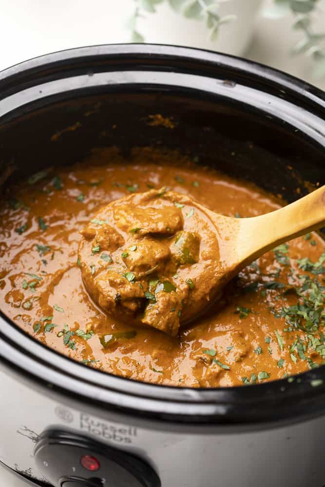 A shot of a ladle-full of yellow tikka masala in a slow cooker