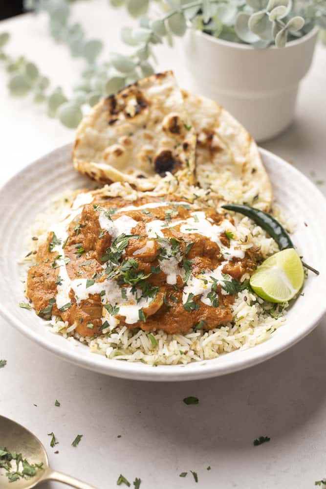 Picture of yellow tikka masala served over jeera rice with naan in a white bowl