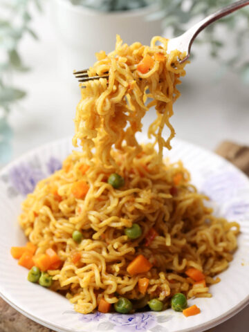 Masala maggi served in a white plate with a steel fork.