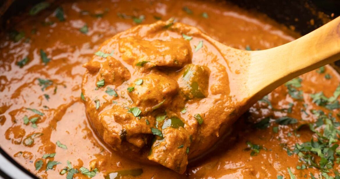 A shot of a ladle-full of chicken tikka masala in a slow cooker