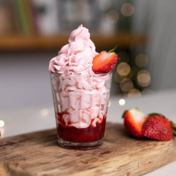 Strawberry mousse layered in a glass with strawberry compote topped with half a strawberry on a wooden board.