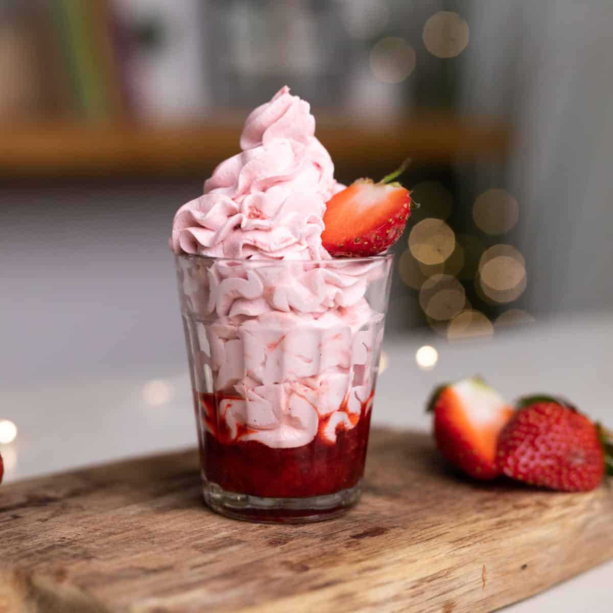 Strawberry mousse layered in a glass with strawberry compote topped with half a strawberry on a wooden board.