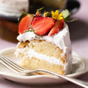 A slice of eggless vanilla cake layered with whipped cream and topped with strawberries