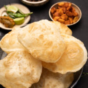 A plate of stacked bhature with a side of fried chilli, fried aloo and chole