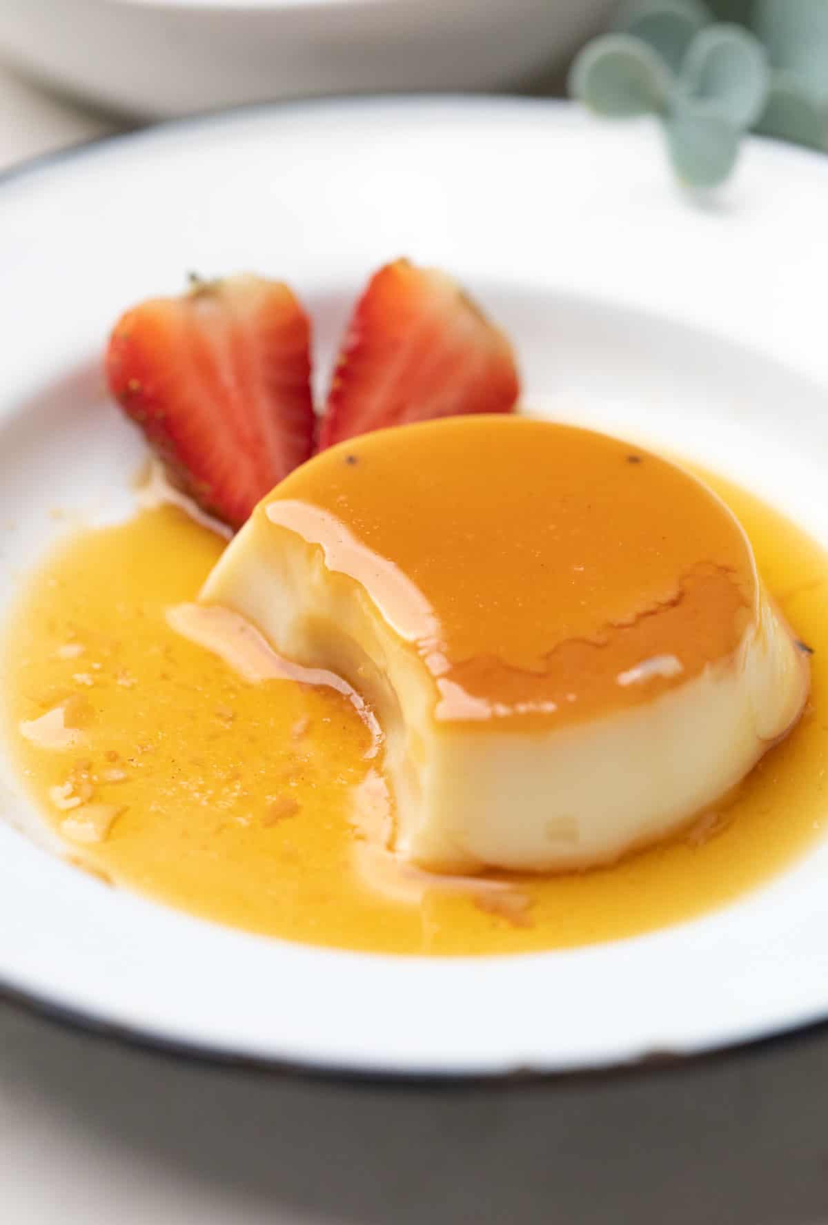 caramel cusstard served on a white plate with strawberries on the side.