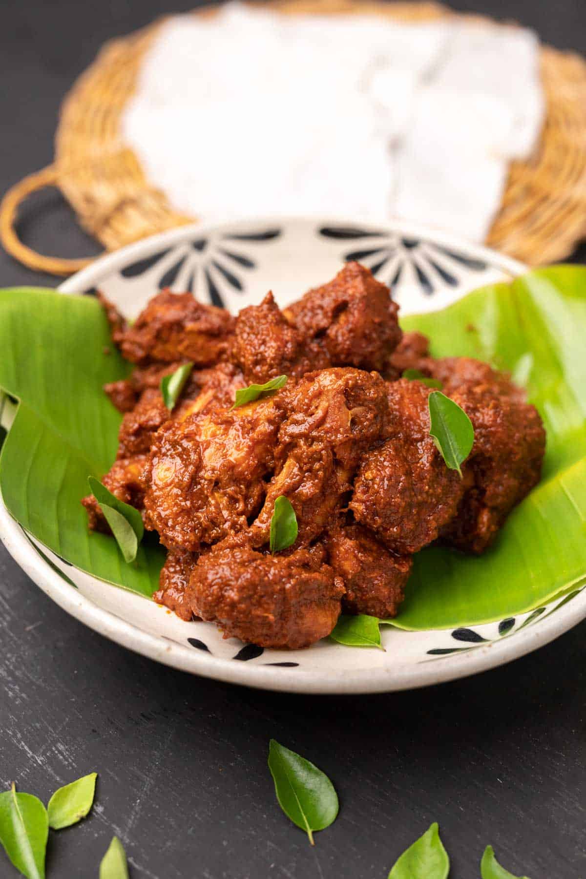 chicken ghee roast served on a white bowl over a plantain leaf