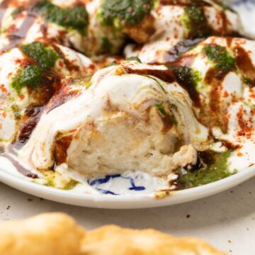 a plate of dahi vada with curd, tamarind chutney and coriander mint chutney drizzled on top.
