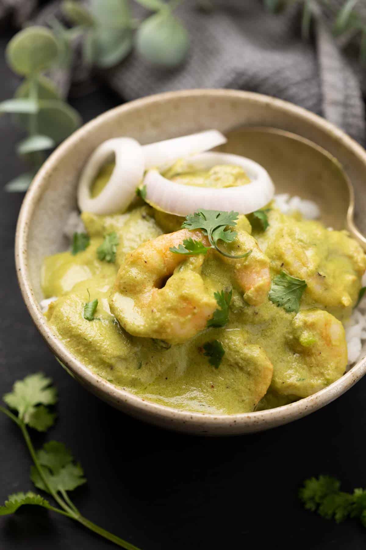 a bowl with white rice topped with green prawn curry with roundels of o