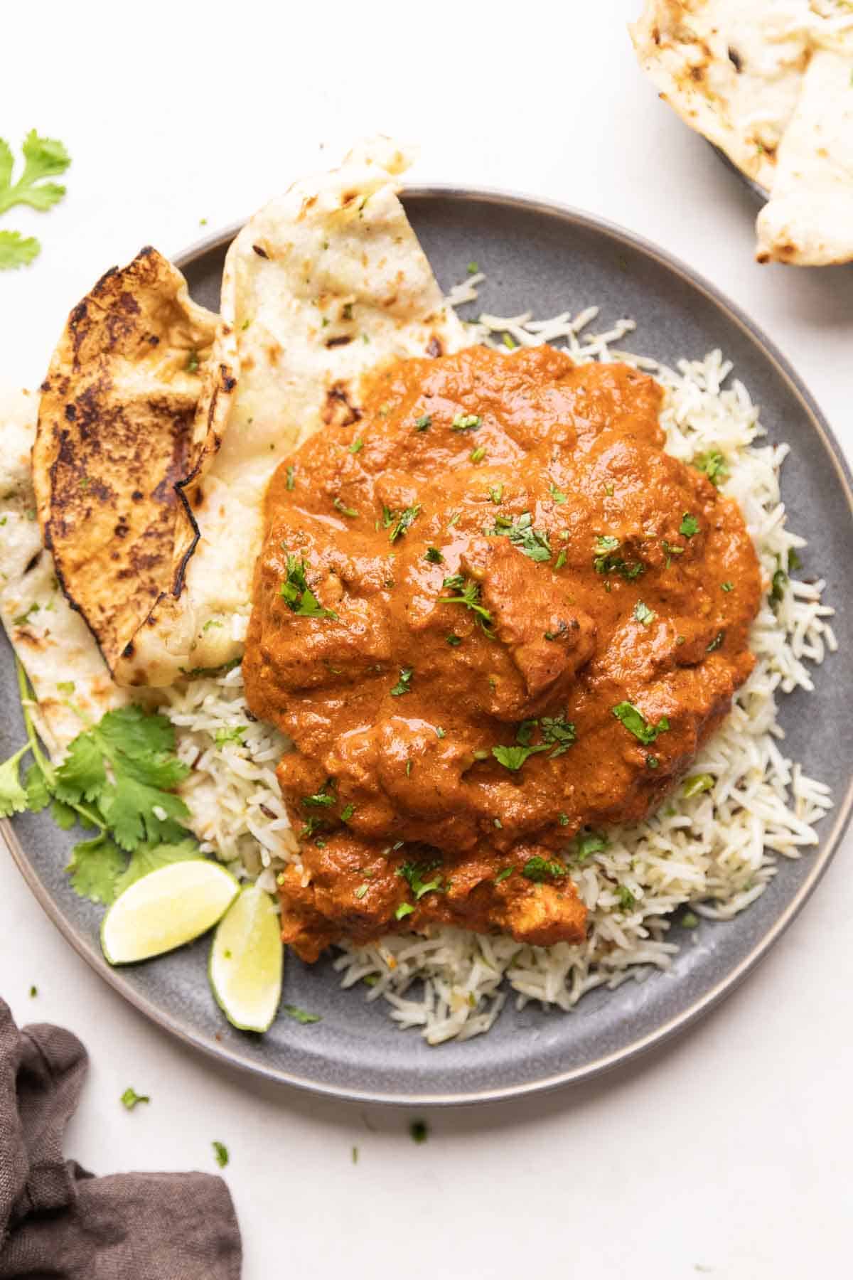 a plate of jeera rice topped with chicken tikka masala with a side of naan