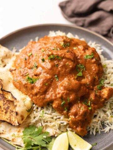 a plate of jeera rice topped with chicken tikka masala with a side of naan
