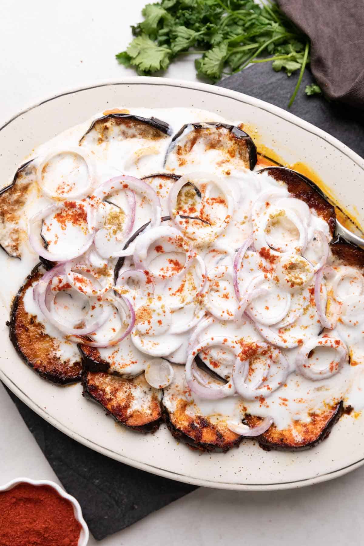 platter with fried eggplant slices and sliced onion topped with a curd mix