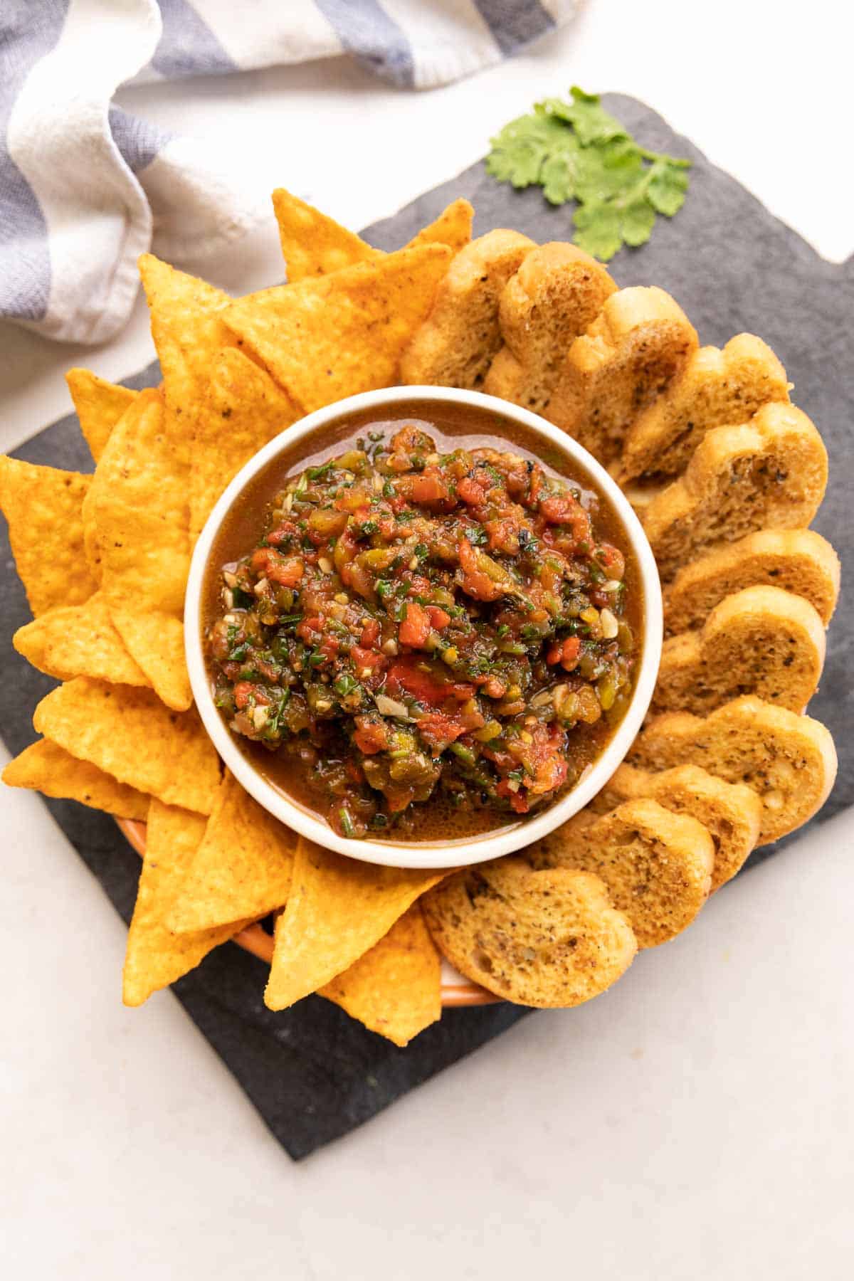 plate of nachos and crostini with a bowl of tomato salsa in the middle 