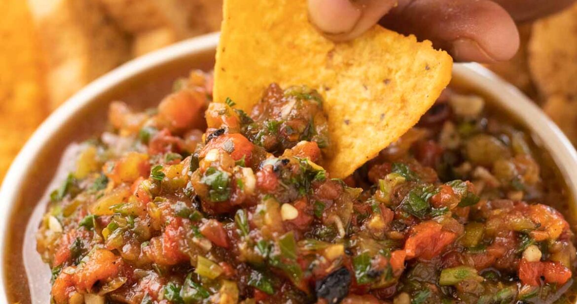 a nacho chip being dipped into a bowl of tomato salsa