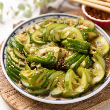 Asian cucumber salad served on a vibrant white and blue plate, featuring sliced Persian cucumbers tossed in a flavourful dressing