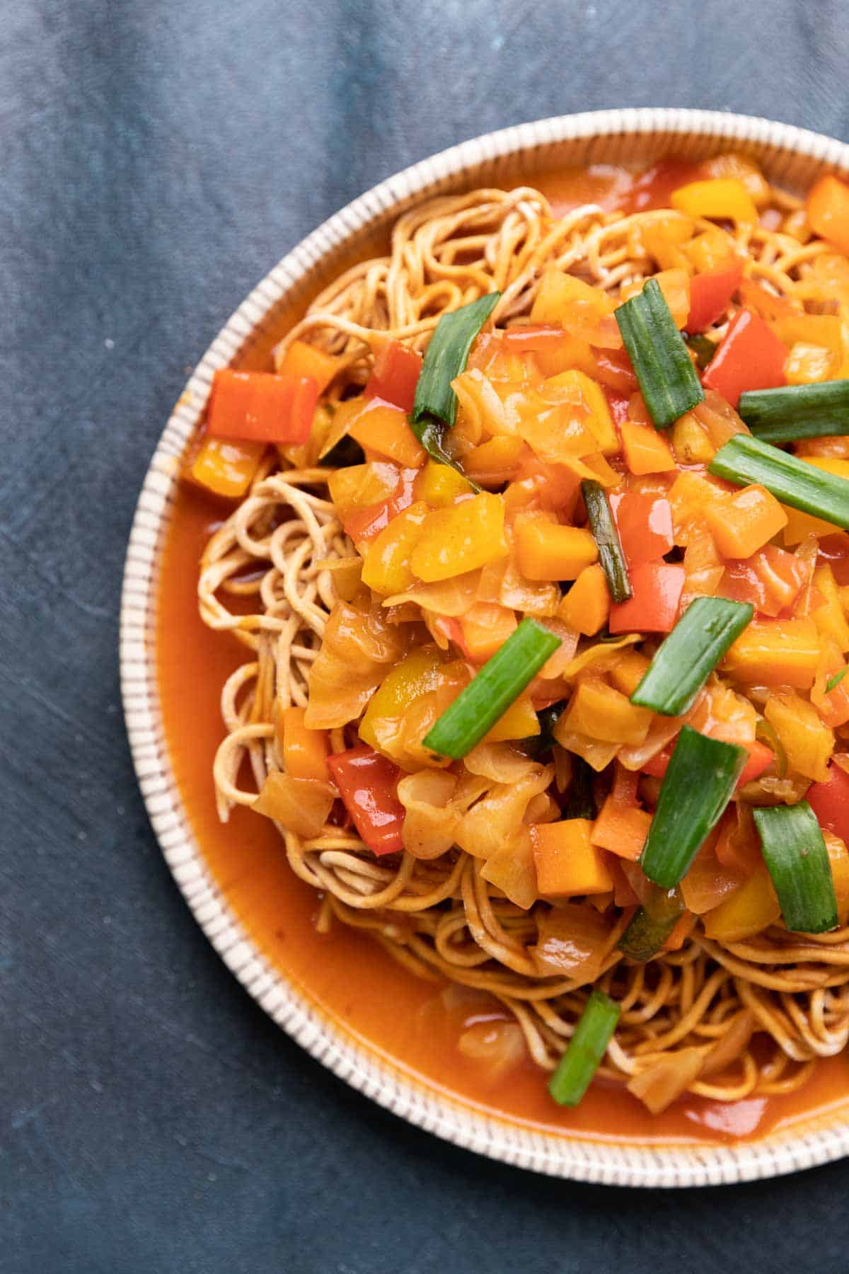 a plate of crispy noodles topped with sweet and sour veggies and garnished with spring onions