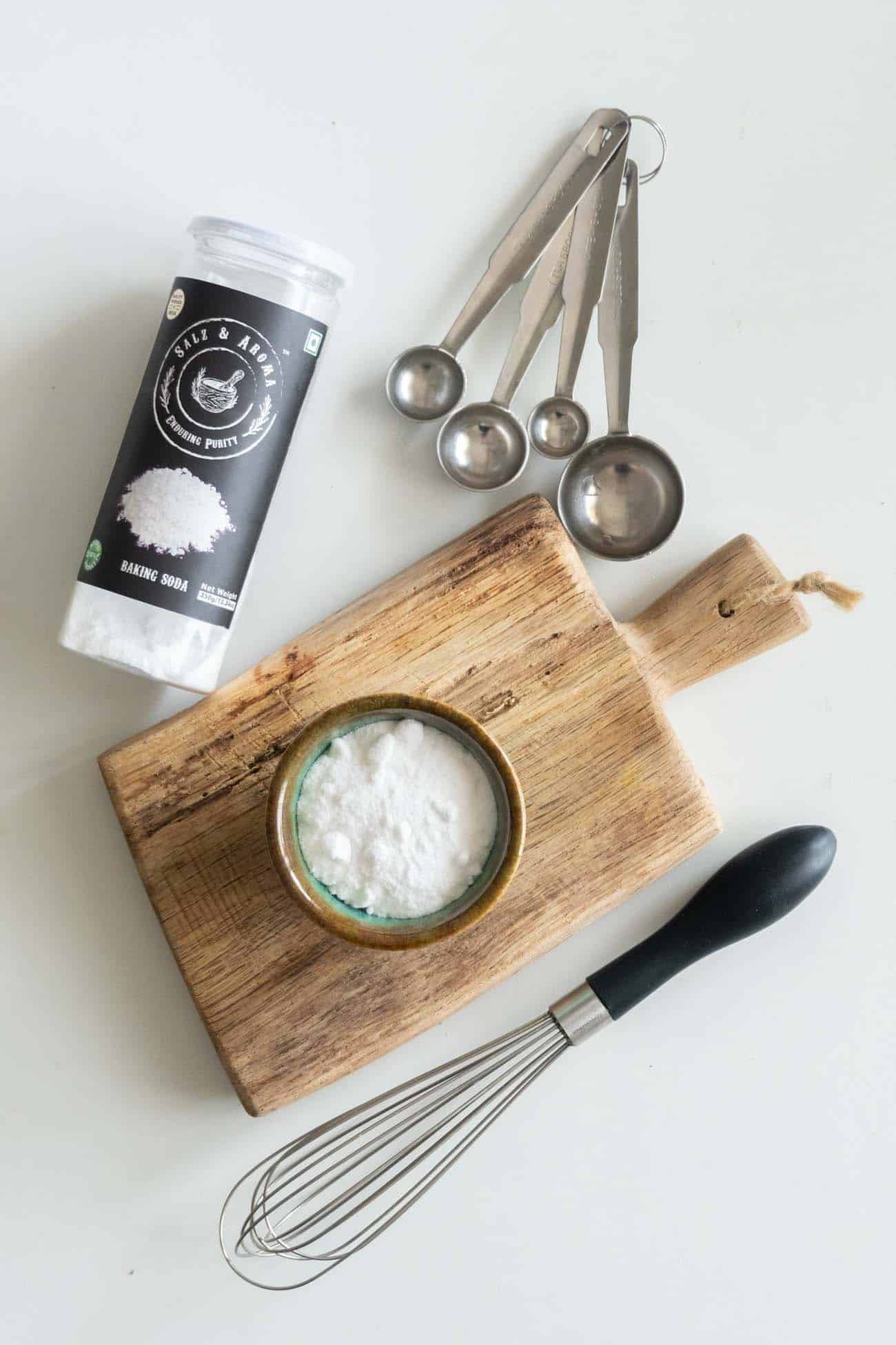 picture of baking soda in a cup on a chopping board with a whisk and measuring spoons on the side