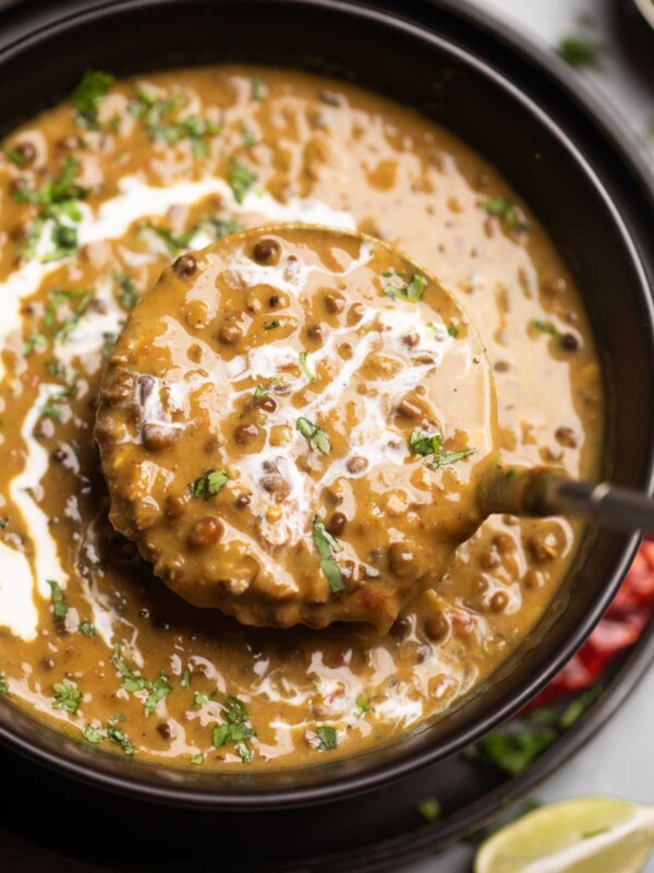A ladleful of creamy amritsari dal coming out of a bowl
