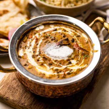 picture of a amritsari dal with cream drizzled on top in a steel copper bowl with rice and roti on the side