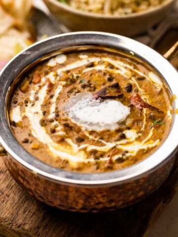 picture of a amritsari dal with cream drizzled on top in a steel copper bowl with rice and roti on the side
