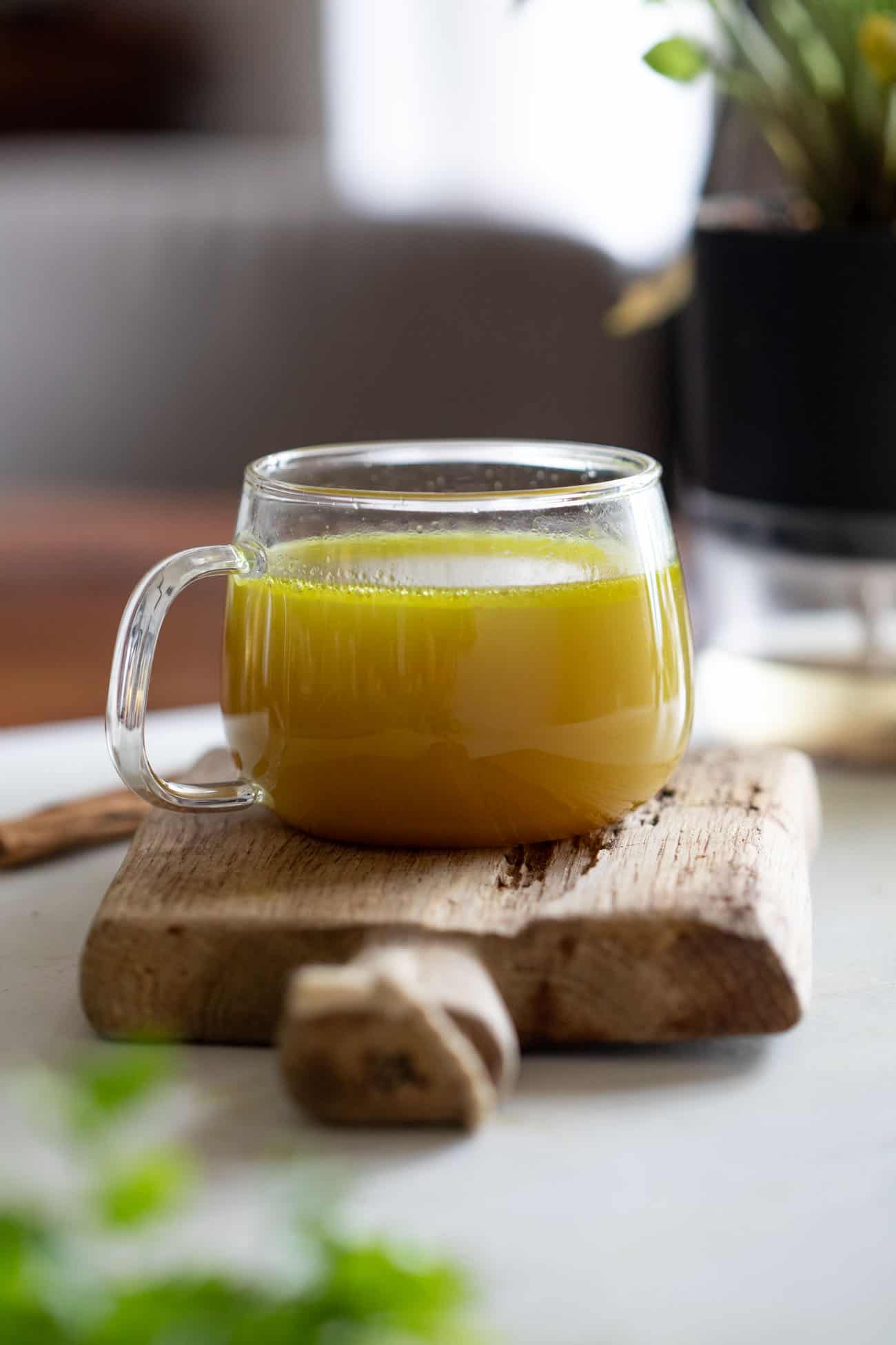 shot of a clear glass mug with turmeric chicken broth resting on a wooden board