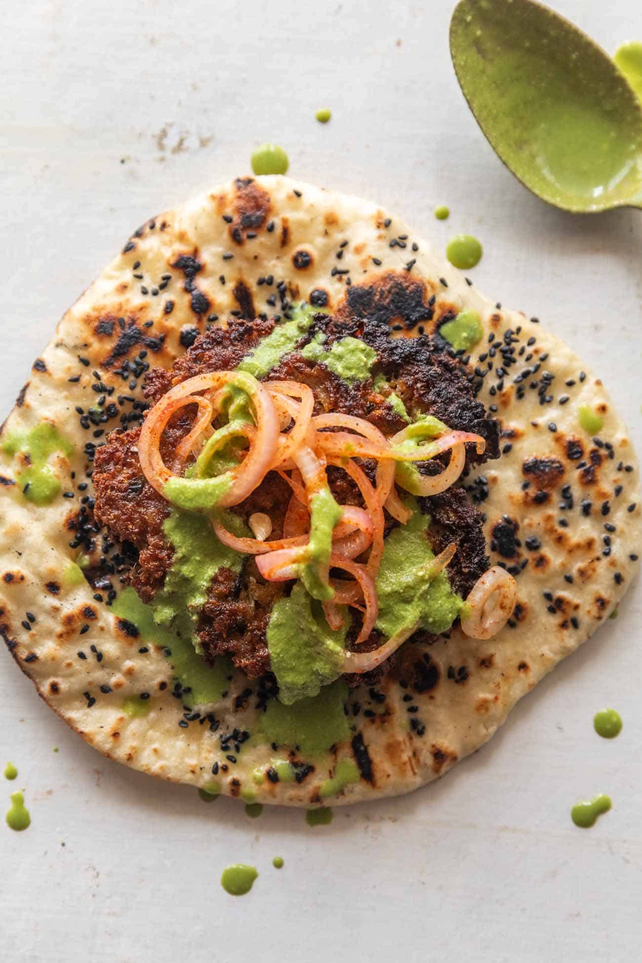 chapli kebab placed on naan with onions and mint chutney, served as a taco